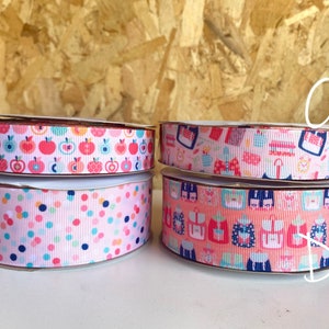 May include: Four rolls of pink and white patterned ribbon with different designs. The designs include apples, polka dots, and school supplies.