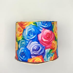May include: A roll of ribbon featuring a vibrant floral pattern of roses in shades of blue, pink, yellow, and orange. The ribbon is wrapped around a cardboard core, perfect for crafts and gift wrapping.