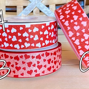 May include: Three rolls of decorative ribbon with heart patterns. The top roll features white hearts on a red background. The middle roll has red hearts on a pink background. The third roll has pink hearts on a red background.