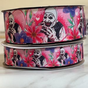 May include: Two spools of pink and white ribbon with a repeating pattern of a creepy clown with a toothy grin, hearts, and flowers.
