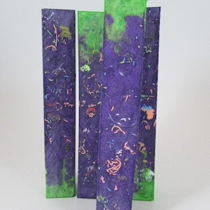 May include: Four long, thin, rectangular pieces of wood with a purple base and green, blue, and pink flecks throughout. The wood is polished and smooth.