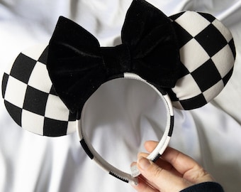 May include: Black and white checkered mouse ears with a black velvet bow. The ears are attached to a black headband.