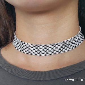 Puede incluir: Un collar choker plateado con piedras cuadradas negras. El collar está hecho de un diseño de cadena.