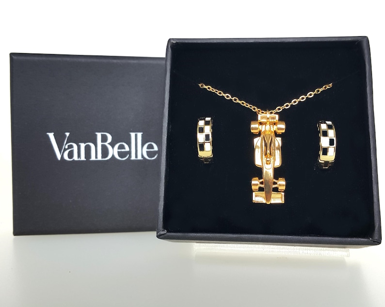 May include: A gold necklace and earring set with a race car pendant and hoop earrings with black and white chequered accents. The set is presented in a black box with the brand name "VanBelle" in white.