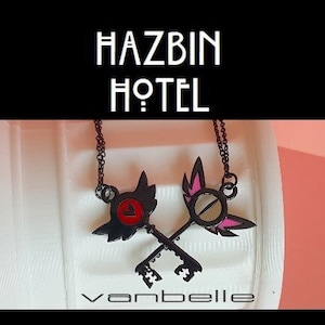 May include: A black pendant necklace featuring two key charms with black and pink detailing. The necklace has a black chain. The words "HAZBIN HOTEL" are at the top, and "vanbelle" is at the bottom of the image.
