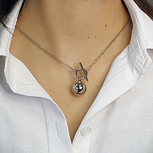 May include: A silver chain necklace with a toggle clasp and a large silver ball pendant.