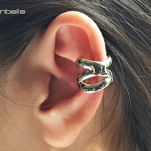 May include: Silver ear cuff with a curved, abstract design. The cuff is worn on the upper part of the ear.