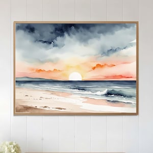 Op de afbeelding: Een rechthoekige ingelijste wandkunstprint met een aquarellandschap van een strand bij zonsondergang. De scène toont een donkere, bewolkte lucht die overgaat in een zachte oranje horizon, een kalme oceaan en een zandstrand in neutrale tinten.