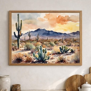 Può includere: Un dipinto ad acquerello incorniciato che raffigura un paesaggio desertico con vari cactus, tra cui un alto saguaro, sullo sfondo di montagne blu in lontananza e un cielo dai toni caldi con nuvole arancioni e gialle sopra un terreno sabbioso.