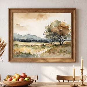 May include: A framed watercolour landscape painting featuring a large tree, rolling hills, and a wooden fence under a soft, muted sky. The artwork is displayed above a wooden dining table with a bowl of apples, a vase of dried wheat, and candles.