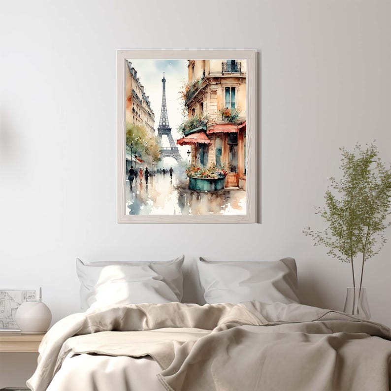 Pode incluir: Uma pintura em aguarela emoldurada que retrata uma cena de rua parisiense com a Torre Eiffel ao fundo. A obra apresenta edif&iacute;cios em tons quentes, um toldo vermelho sobre uma montra e silhuetas de pessoas a caminhar numa rua molhada.