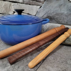 May include: Three wooden kitchen utensils, one dark brown, one light brown, and one natural wood color, are arranged on a gray stone surface next to a blue enameled cast iron pot.
