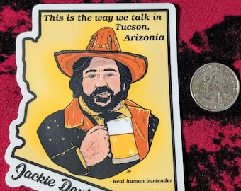 May include: A die-cut sticker shaped like the state of Arizona featuring an illustration of a bearded person in a cowboy hat holding a beer mug. Text reads: This is the way we talk in Tucson, Arizonia, Jackie Daytona, and - Real human bartender.