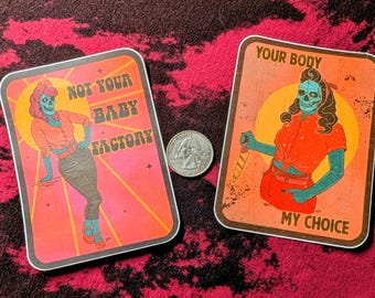 May include: Two rectangular stickers featuring teal-skinned figures with skull faces. The left sticker reads NOT YOUR BABY FACTORY with a figure in a pink top. The right sticker reads YOUR BODY MY CHOICE with a figure holding a knife. A US quarter is shown.