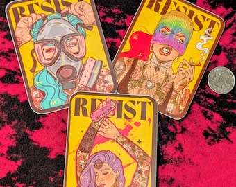 May include: Three rectangular stickers with the word RESIST printed at the top. One shows a person in a gas mask with blue hair, another a person in a rainbow balaclava smoking, and the third a person with purple hair holding a pink spray can.