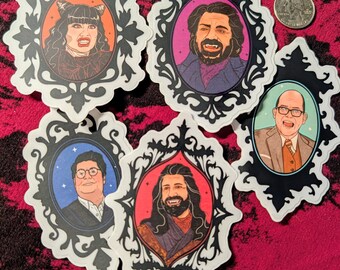 May include: Five die-cut stickers featuring illustrated portraits of characters in ornate black frames. The stickers depict four individuals with varied expressions and one individual with fangs. A US quarter coin is included for scale reference.