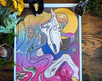 May include: A fantasy art print featuring a horse skull with flowing, rainbow-colored hair. The artwork includes a yellow moon, mushrooms, and a vibrant color palette of blues, purples, and pinks. The print is surrounded by decorative flowers and moss.