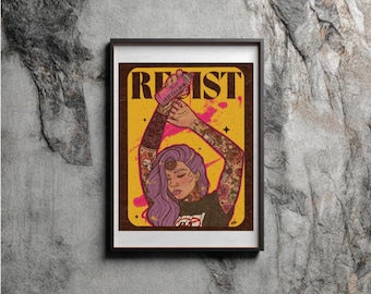 May include: A framed art print featuring a person with purple hair and tattoos on both arms, holding a pink spray paint can above their head. The background is yellow with a brown border and the word RESIST printed in bold black letters at the top.