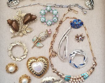 May include: A collection of vintage jewellery featuring a variety of styles, including a leaf-shaped necklace, a heart-shaped pendant, a floral brooch, and a ring with a pearl centre.