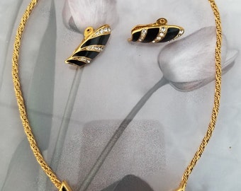 May include: A gold chain necklace with a black enamel and rhinestone pendant. Matching black enamel and rhinestone clip-on earrings.