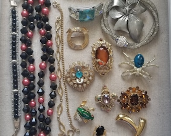 May include: A collection of vintage jewellery including necklaces, bracelets and brooches. The jewellery features a variety of colours, including black, red, gold, silver and green. Some of the pieces are adorned with rhinestones, pearls and other decorative elements.