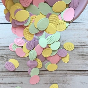 May include: A large pile of pastel-coloured paper Easter eggs with different embossed designs. The eggs are in shades of pink, yellow, green, and purple.