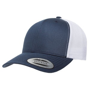 May include: A navy blue and white trucker hat with a mesh back. The hat has a curved brim and a snap closure. The hat has a label that says "The Classics" and "Snapback" with the text "Yupoong - Since 1974" underneath.