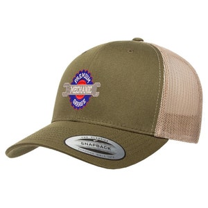 May include: A green and beige trucker hat with a logo that says "Premium Mechanic Garage" in a circle with a wrench. The hat has a mesh back and a snap closure.