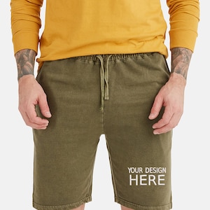 May include: A pair of olive green drawstring shorts with the text "YOUR DESIGN HERE" printed in white on the right leg.