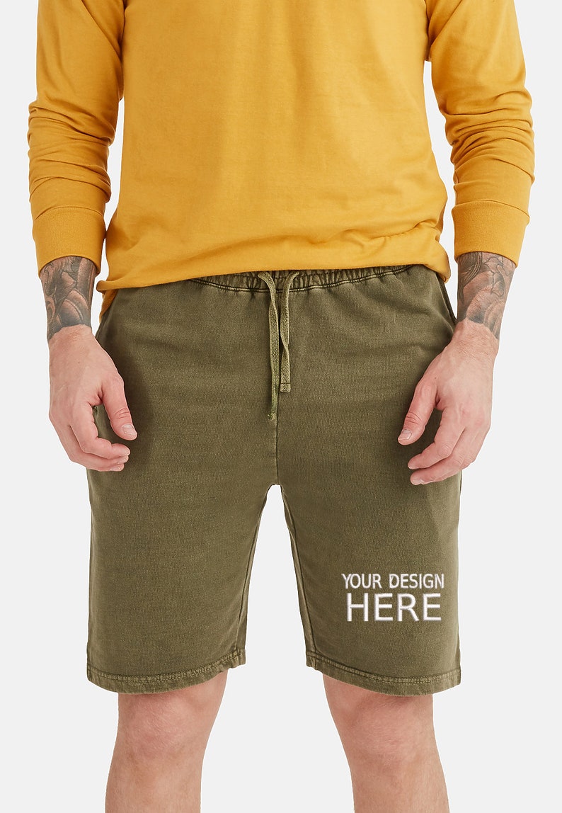 May include: A pair of olive green drawstring shorts with the text "YOUR DESIGN HERE" printed in white on the right leg.