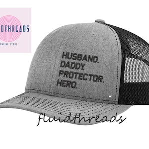 May include: Gray and black trucker hat with the text "Husband. Daddy. Protector. Hero." embroidered in black.