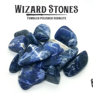 May include: A collection of tumbled polished sodalite stones. The stones are a deep blue color with white veins running through them. The stones are arranged in a pile on a white background. The text "WIZARD STONES" and "TUMBLED POLISHED SODALITE" is visible above the stones.