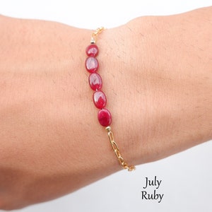 Puede incluir: Un brazalete de cadena dorada con piedras preciosas de rubí de forma ovalada roja. El brazalete está en la muñeca de una persona. Julio Rubí.