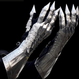 May include: Silver metal gauntlets with articulated fingers and sharp, claw-like tips. The armour features intricate engraved patterns and is designed to cover the hands and forearms. The "Battle Queen Armory" logo is visible in the upper left corner.