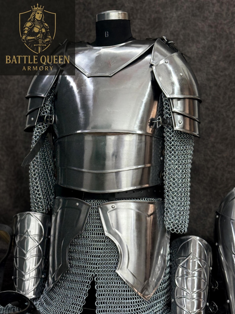May include: A full suit of polished steel armor, including a breastplate, shoulder guards, and leg protection. Chainmail sleeves and lower body protection are also visible. The armor is displayed on a mannequin, showcasing its medieval design.