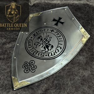 Puede incluir: Un escudo plateado con una cruz negra y un emblema circular con dos caballeros a caballo. El escudo tiene esquinas de lat&oacute;n y es de Battle Queen Armory.