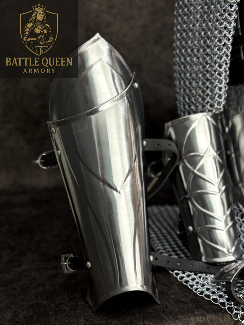 May include: Polished steel arm guards with decorative etched lines and leather straps. The arm guards are part of a set of armor. The Battle Queen Armory logo is visible in the upper left corner.