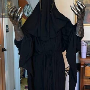 May include: A black hooded robe with metal claw gauntlets. The gauntlets have long, sharp claws and are attached to a leather-like glove. The robe is long and flowing, with a high collar. The Battle Queen Armory logo is visible in the upper left corner.