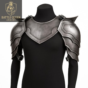 May include: A set of silver-colored shoulder armor, featuring layered plates and a central chest piece. The armor is displayed on a black mannequin, showcasing its design and structure. The Battle Queen Armory logo is visible in the upper left corner.