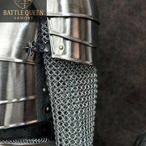 May include: Close-up of medieval armor, featuring polished metal plates and chainmail. The armor includes a shoulder guard and a section of chainmail, with the "BATTLE QUEEN ARMORY" logo visible in the upper left corner.