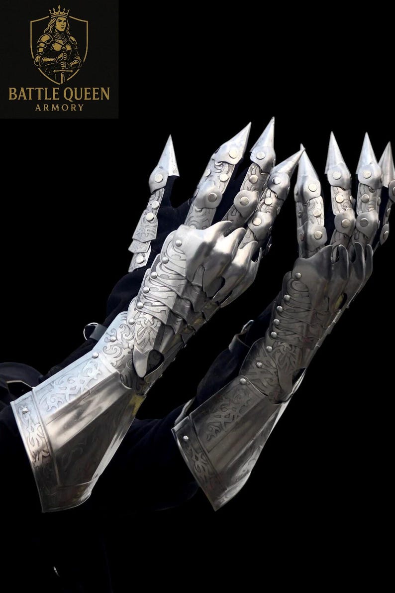 May include: Silver metal gauntlets with articulated fingers and sharp, claw-like tips. The armour features intricate engraved patterns and is designed to cover the hands and forearms. The "Battle Queen Armory" logo is visible in the upper left corner.
