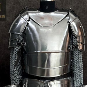 May include: A polished, silver-colored suit of armor, displayed on a mannequin. The armor includes a chest plate, shoulder guards, and chainmail. The logo "BATTLE QUEEN ARMORY" is visible in the upper left corner.