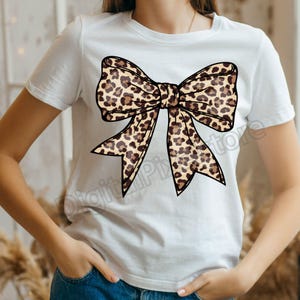 May include: White t-shirt with a large brown and black leopard print bow.