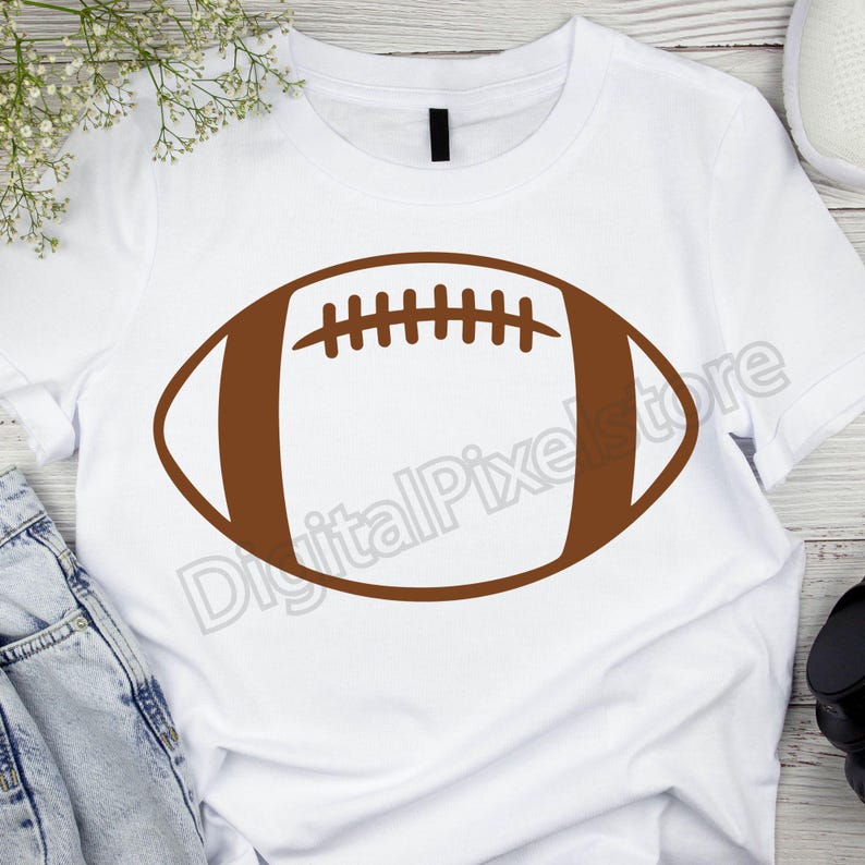 Pode incluir: Uma camiseta branca com um contorno marrom de uma bola de futebol americano.
