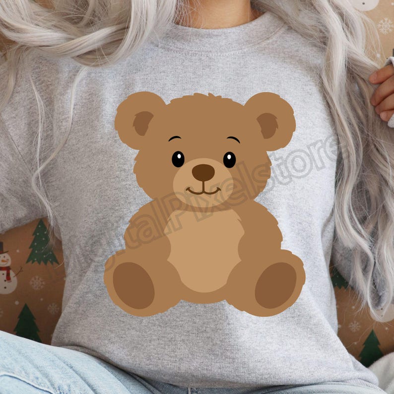 May include: A light gray sweatshirt featuring a cartoon teddy bear illustration. The bear is brown with a lighter brown belly and paws, and has a smiling face with black eyes. The sweatshirt is a casual style.