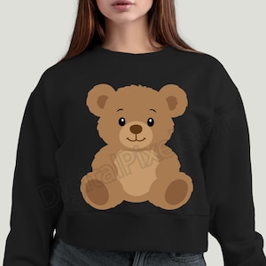 May include: Black sweatshirt featuring a cartoon teddy bear illustration. The bear is brown with a light brown belly and paws, a black nose, and a smiling expression. The design is centered on the front of the sweatshirt.
