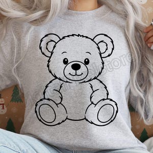 May include: A light gray sweatshirt featuring a black outline of a teddy bear. The bear has a smiling face, round ears, and is sitting with its arms and legs outstretched. The design is centered on the front of the sweatshirt.