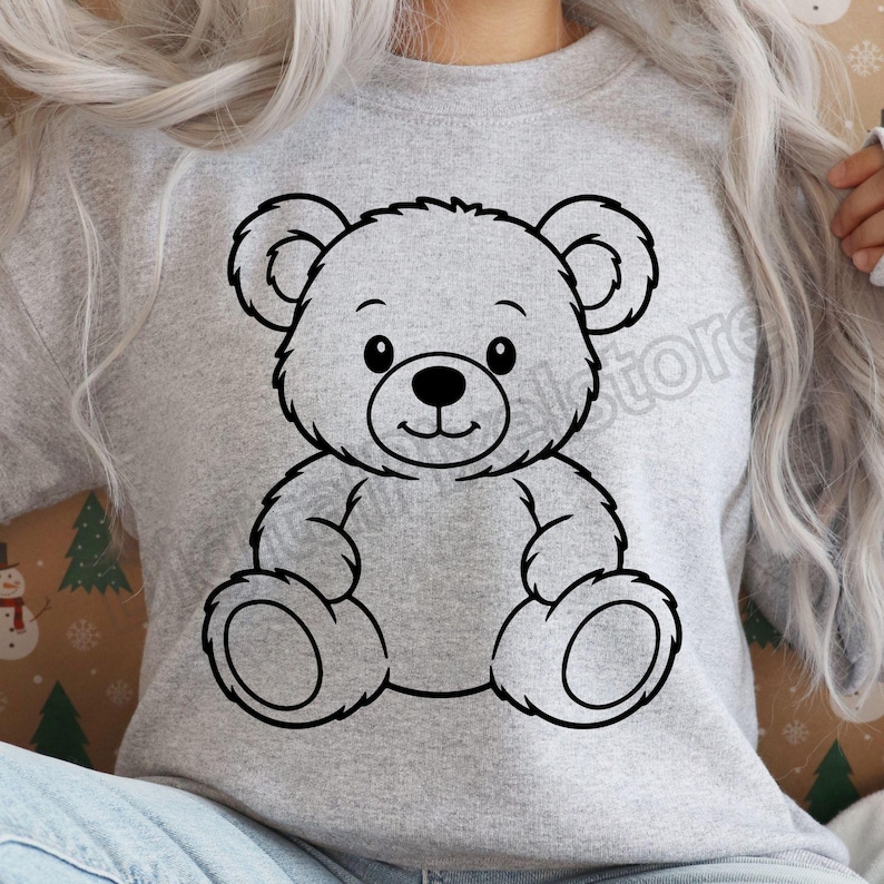 May include: A light gray sweatshirt featuring a black outline of a teddy bear. The bear has a smiling face, round ears, and is sitting with its arms and legs outstretched. The design is centered on the front of the sweatshirt.