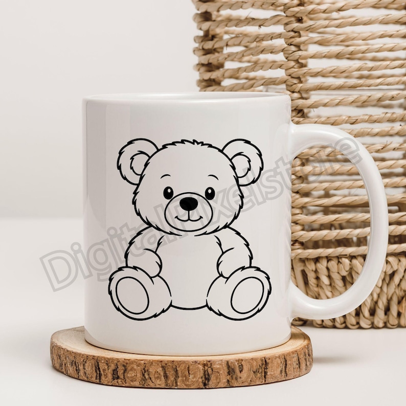 May include: White ceramic mug featuring a black outline illustration of a teddy bear. The bear has a smiling face and is sitting. The mug is on a wooden coaster. A woven basket is in the background.