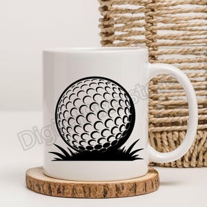 May include: White ceramic mug featuring a black golf ball design with grass detail. The golf ball is a detailed graphic, set against a white background. The mug sits on a wooden coaster, with a woven basket in the background.